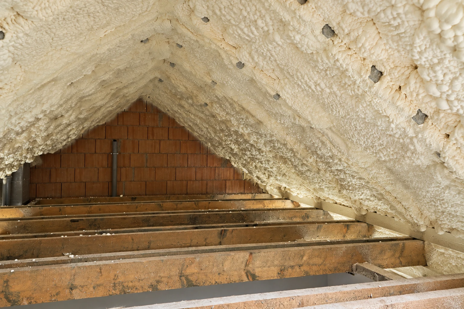 Roof rafters and attic gable coated with thick, uneven cream-colored spray foam.