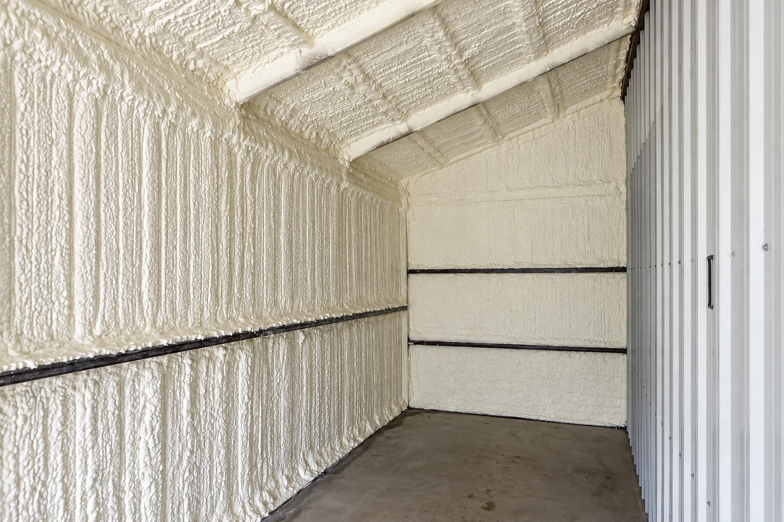 Spray foam insulation covers the walls and ceiling of a commercial metal-sided space with a concrete floor.