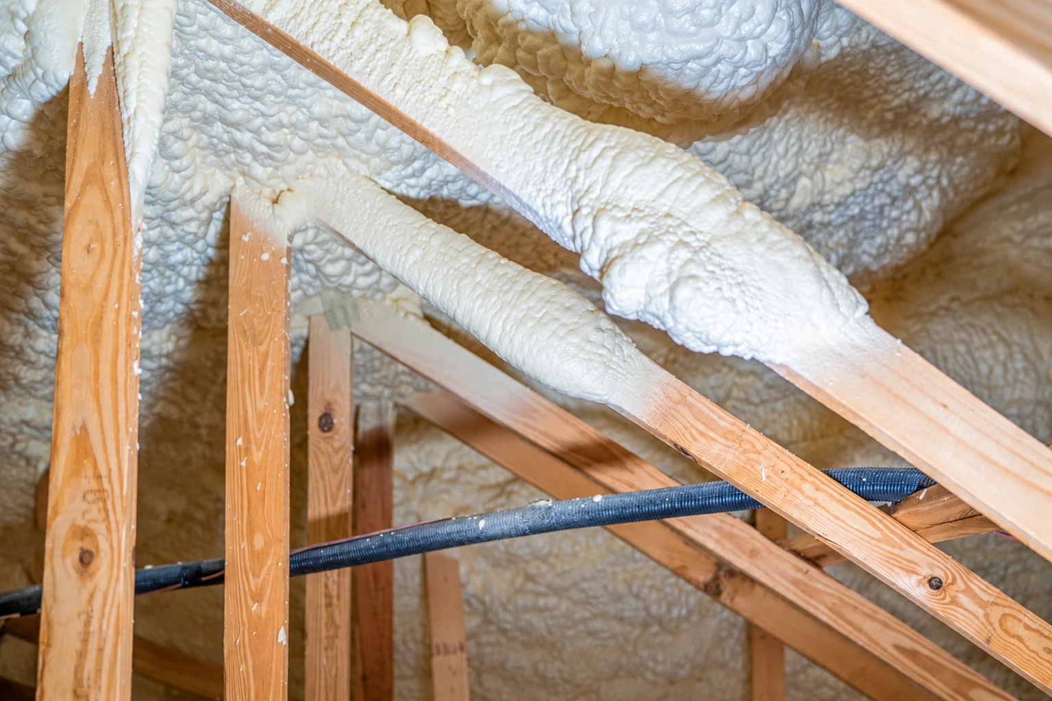 White spray foam coats the roof and rafters of a wooden attic.
