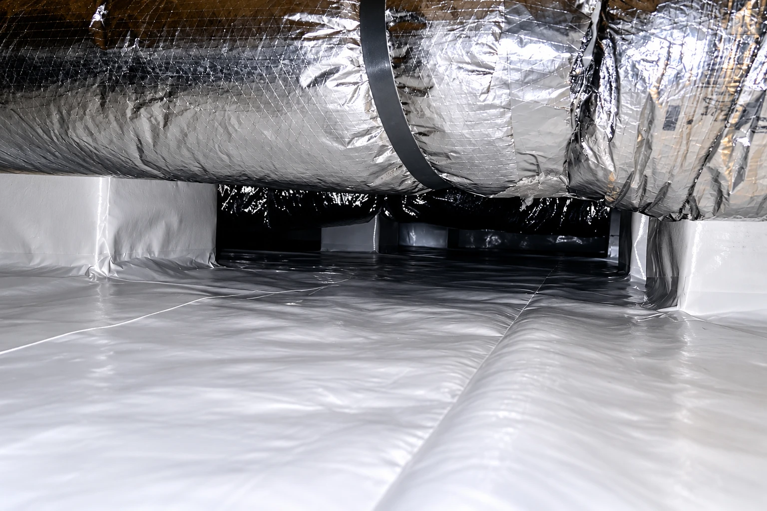 A crawl space floor and lower walls are covered with reflective plastic vapor barrier beneath insulated ductwork.