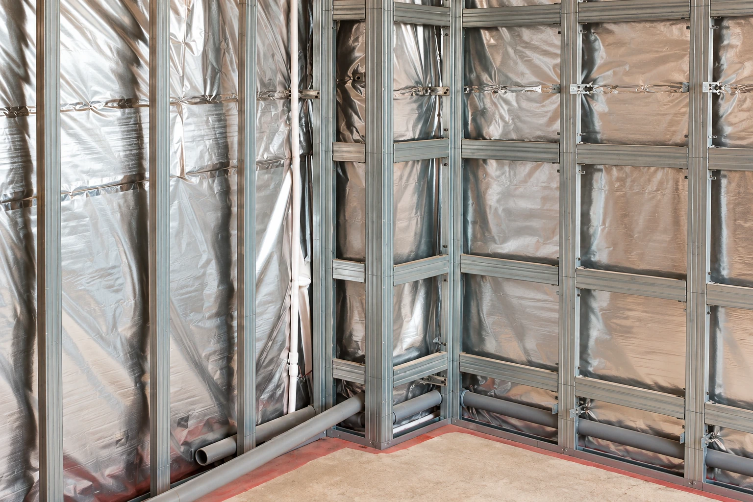 Metal wall framing encloses reflective insulation and pipes in an unfinished room.